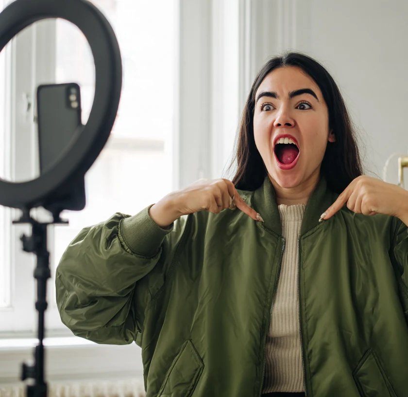 Vendedora mostrando una chaqueta bomber a la cámara durante un live, con el celular en el trípode y el aro de luz encendido